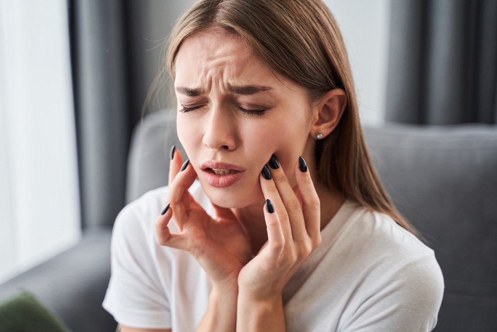 Young woman touching her mouth in pain from a dental emergency, in need of care.