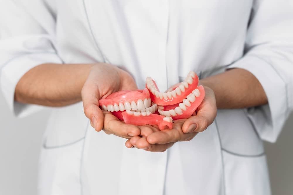 Close up of a dental provider holding a few pairs of dentures in their palms.
