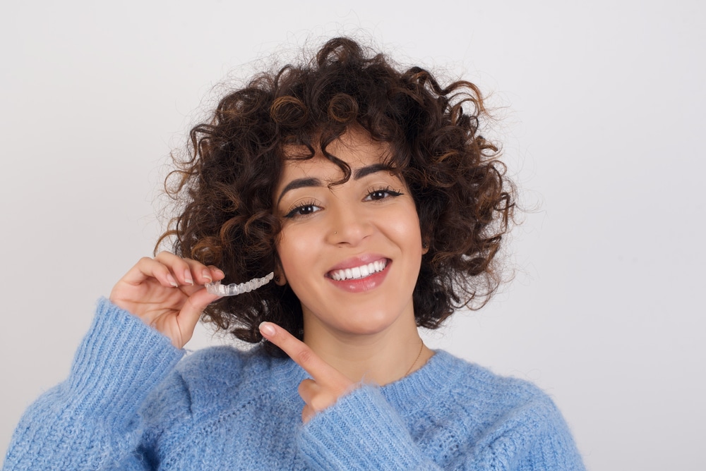 Woman smiling and pointing at her Invisalign aligners, making sure to keep a regular schedule.