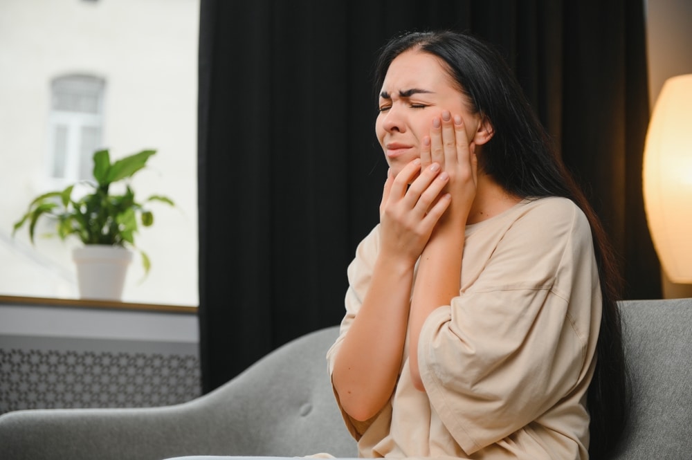 Woman sitting on couch and clutching her mouth in pain from a dental abscess, a serious infection.